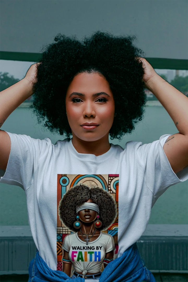 Woman wearing a white t-shirt with a graphic of another woman with an afro and 'Walking by Faith' text.
